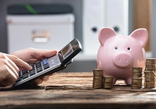 Hand operates calculator near piggy bank