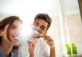 Couple preventing dental emergencies in Ware by brushing teeth