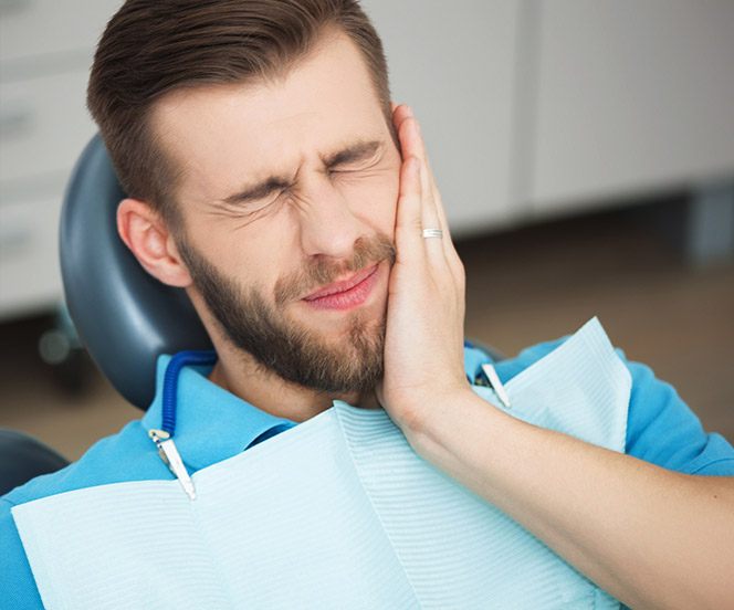 Man in dental chair holding cheek