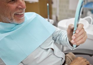 Senior patient holding mirror, looking at his teeth