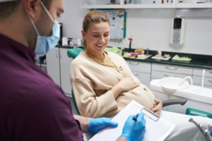 Pregnant women smiling as dentist fills out dental insurance paperwork